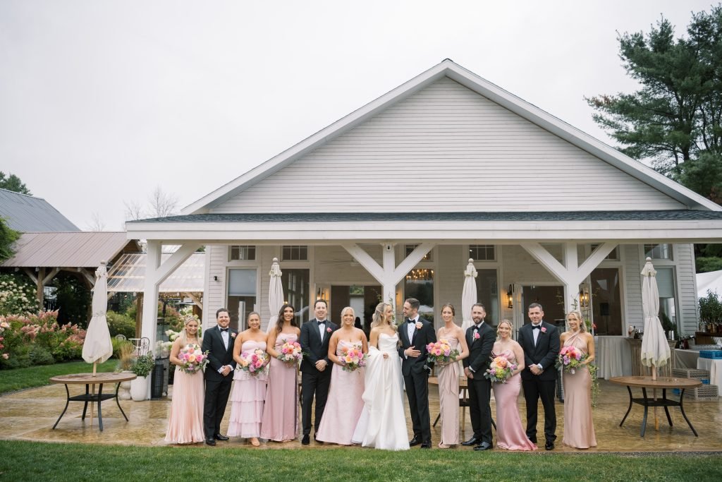 Wedding party posing outside a charming venue with a white porch and lush greenery.