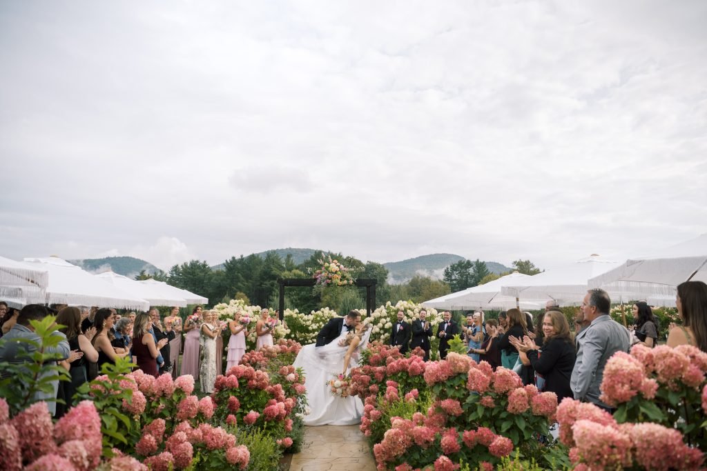 A wedding ceremony in a lush outdoor setting, surrounded by vibrant pink flowers.