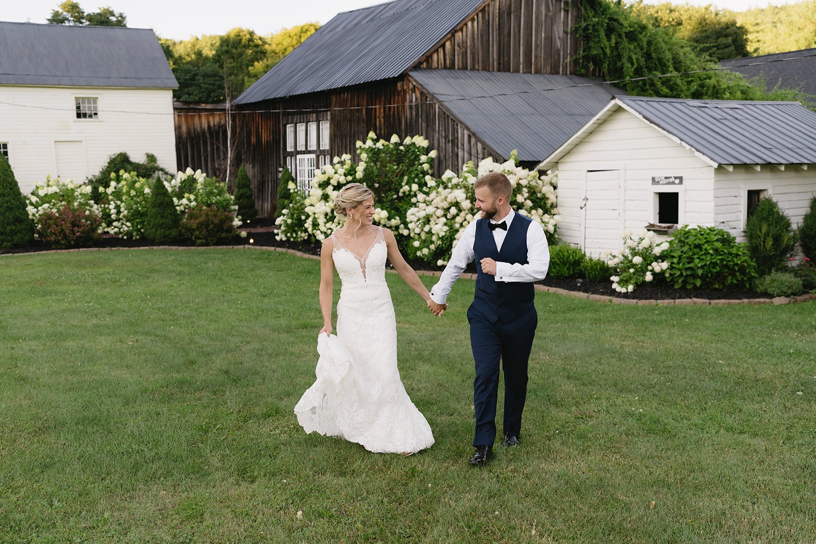 A newlywed couple walks hand-in-hand across a grassy area, smiling and enjoying the moment.