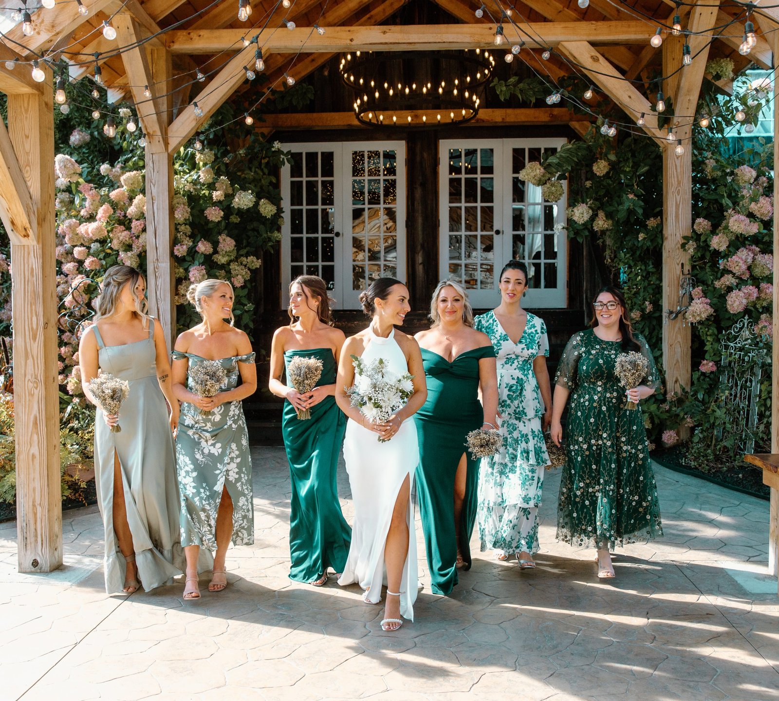 A group of bridesmaids walks together under a charming wooden gazebo adorned with flowers.